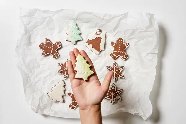 Hand holding a freshly baked cookie in form of Christmas tree. Top view