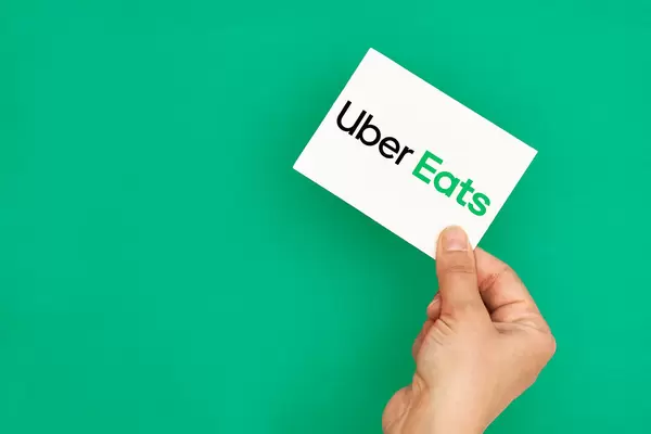 Hand holding a logo of famous takeaway delivery service Uber Eats on green background
