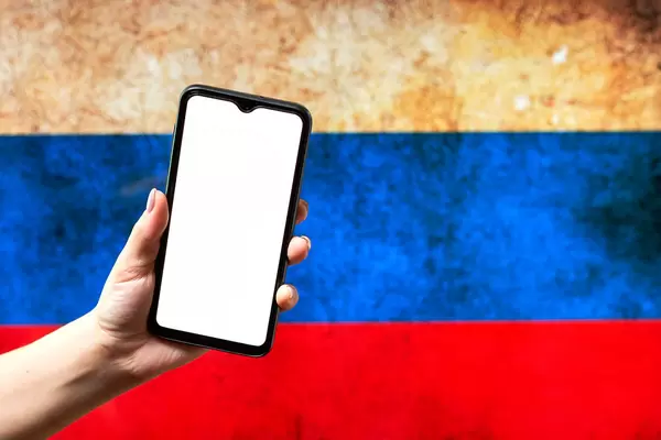 Hand holding a smartphone with a blank screen over the Russian flag