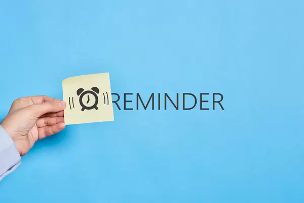 Hand holding a sticky note with ringing alarm clock picture over reminder text