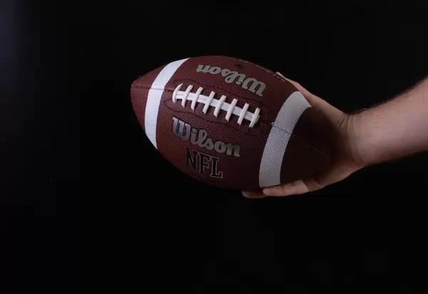 Hand holding american football ball on black background