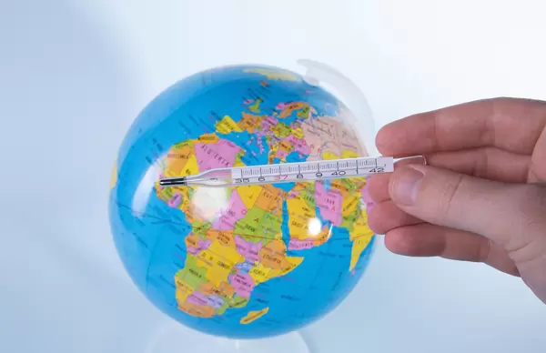 Hand holding analog thermometer over globe