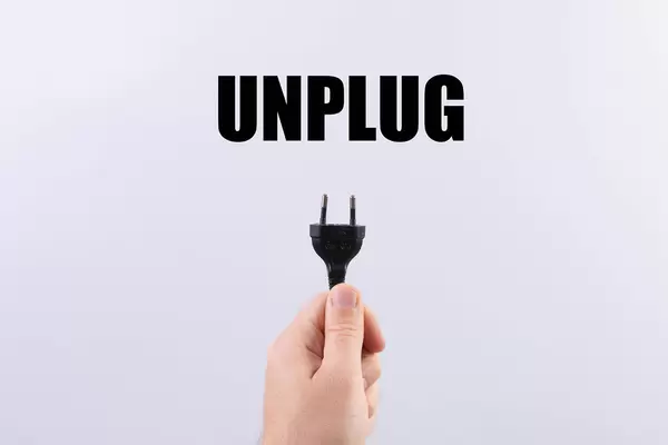 Hand holding black electric European plug isolated on white background with #unplug text