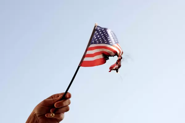 Hand holding burning the American flag - a symbol of mass protests in the USA