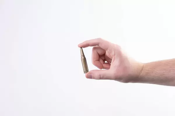 Hand holding caliber bullet against white background