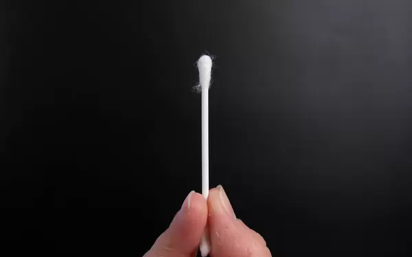 Hand holding cotton swab on a black background