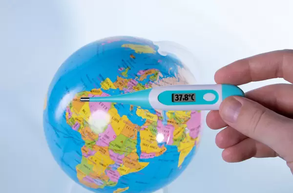 Hand holding digital thermometer over a globe