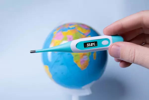 Hand holding digital thermometer showing 37,0°C temperature over a globe