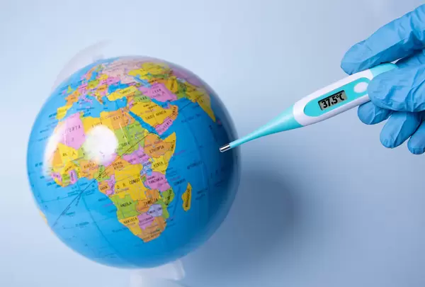 Hand holding digital thermometer showing 37,5°C temperature over a globe