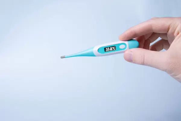 Hand holding digital thermometer showing 37,8°C temperature