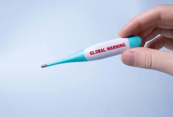 Hand holding digital thermometer with Global warning text
