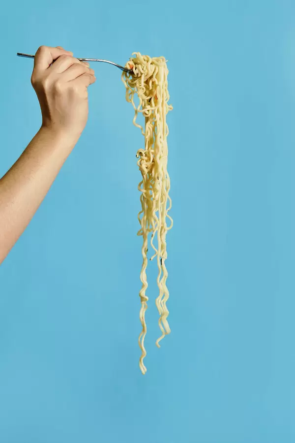 Hand holding fork with insant noodles on bright blue background