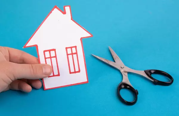 Hand holding house made out of paper with scissors
