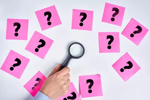 Hand holding magnifying glass among a lot of questions. Finding answers to questions and solving problems