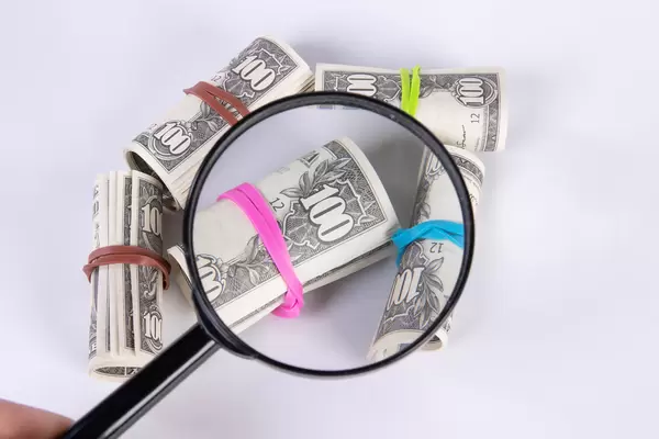 Hand holding magnifying glass over US dollar bills in rolls