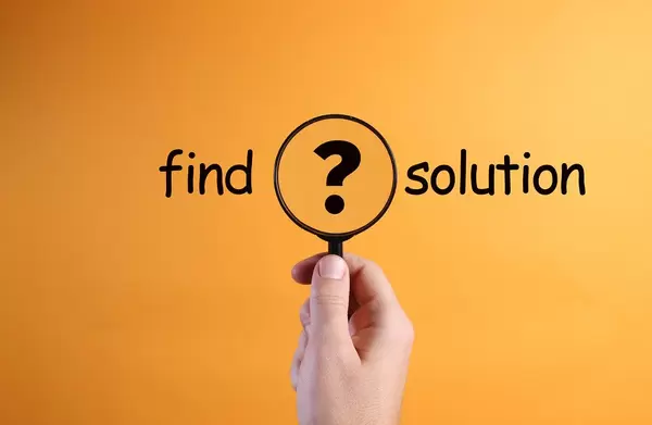 Hand holding magnifying glass with Find solution text on orange background