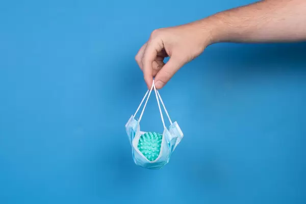 Hand holding medical face mask with Coronavirus bacteria over blue background