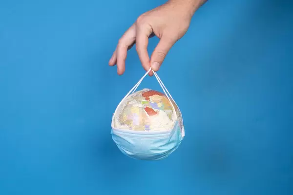 Hand holding medical face mask with globe over blue background