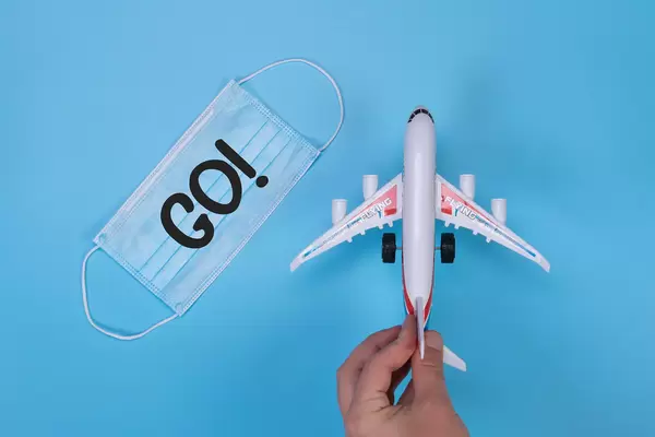 Hand holding miniature airplane and medical face mask with GO! text on blue background