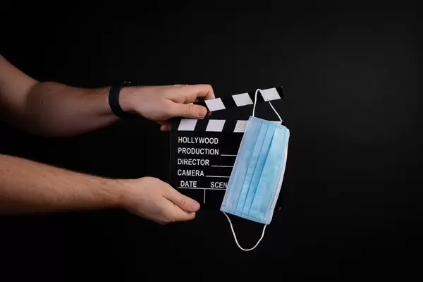 Hand holding movie clapper and medical face mask on black background