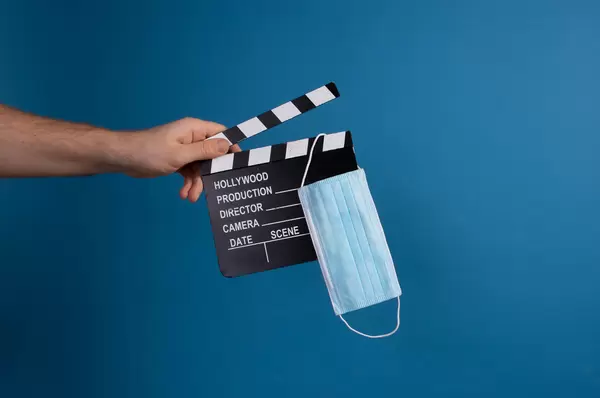 Hand holding movie clapper and medical face mask on blue background