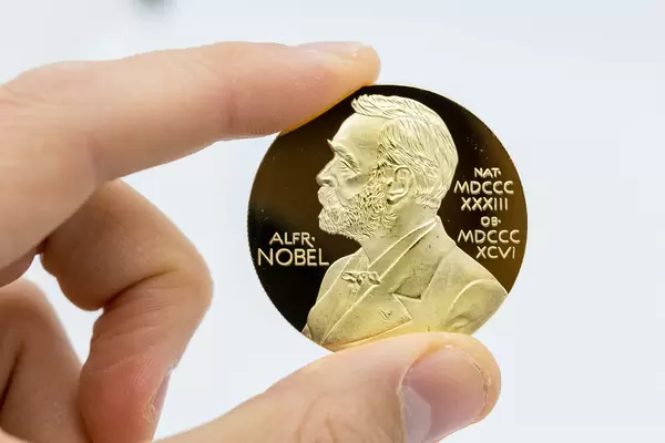 Hand holding Nobel Prize gold medal with the picture of Alfred Nobel against white background