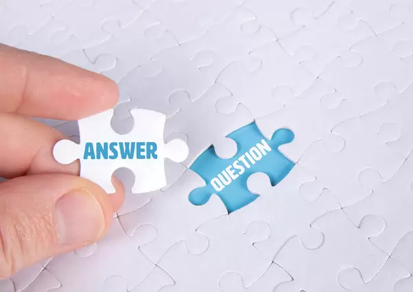 Hand holding piece of jigsaw puzzle with word answer & question