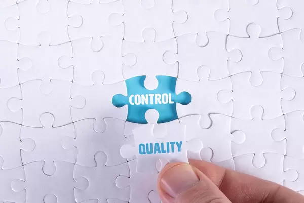 Hand holding piece of jigsaw puzzle with word control & quality