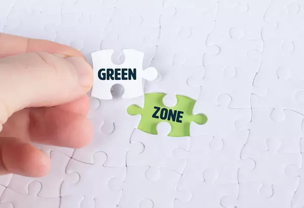 Hand holding piece of jigsaw puzzle with word green & zone