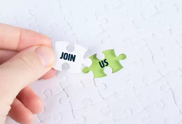 Hand holding piece of jigsaw puzzle with word join & us