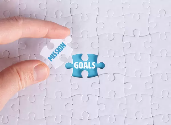 Hand holding piece of jigsaw puzzle with word mission & goals