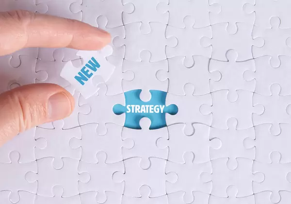 Hand holding piece of jigsaw puzzle with word new & strategy