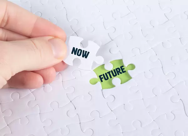 Hand holding piece of jigsaw puzzle with word now & future