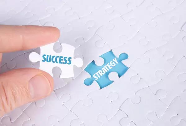 Hand holding piece of jigsaw puzzle with word success & strategy