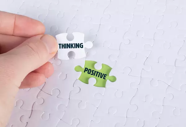 Hand holding piece of jigsaw puzzle with word thinking & positive