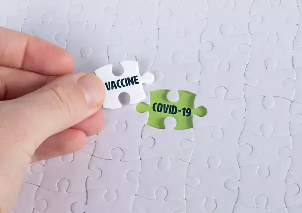 Hand holding piece of jigsaw puzzle with word vaccine & covid-19