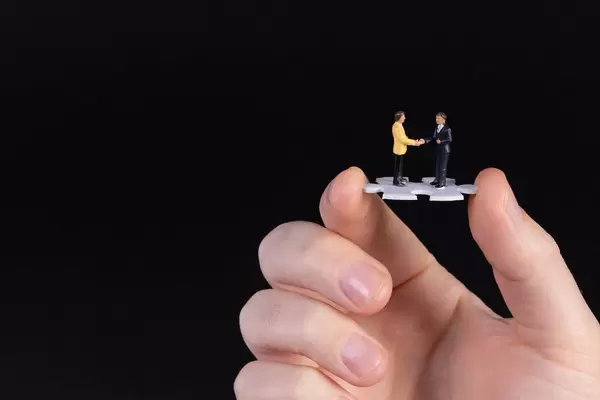 Hand holding puzzle piece with two businessman shaking hands