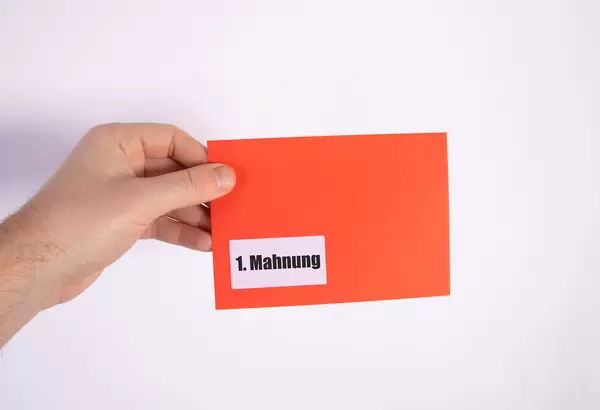 Hand holding red envelope with 1. Mahnung text