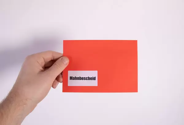 Hand holding red envelope with Mahnbescheid text