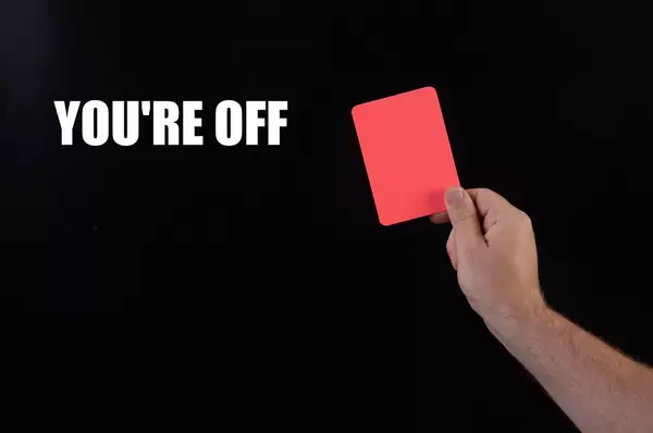 Hand holding red referee card with You're off text on black background