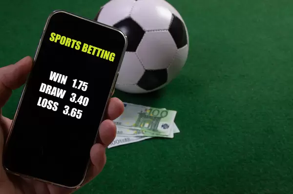 Hand holding smartphone with game betting odds over a soccer ball and Euro banknotes