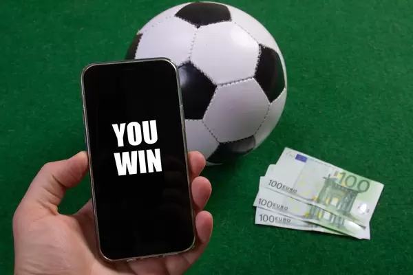 Hand holding smartphone with You Win text over a soccer ball and Euro banknotes