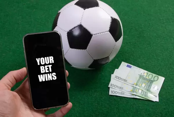 Hand holding smartphone with Your Bet Wins text over a soccer ball and Euro banknotes