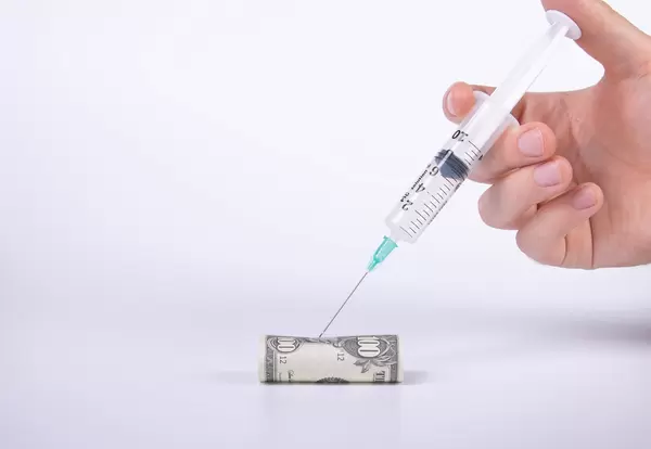 Hand holding syringe over dollar money