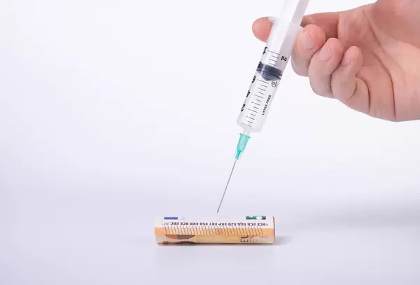Hand holding syringe over euro money