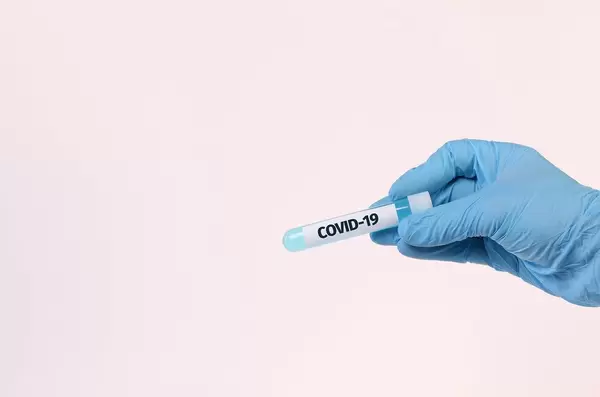 Hand holding test tube with text COVID-19 on white background