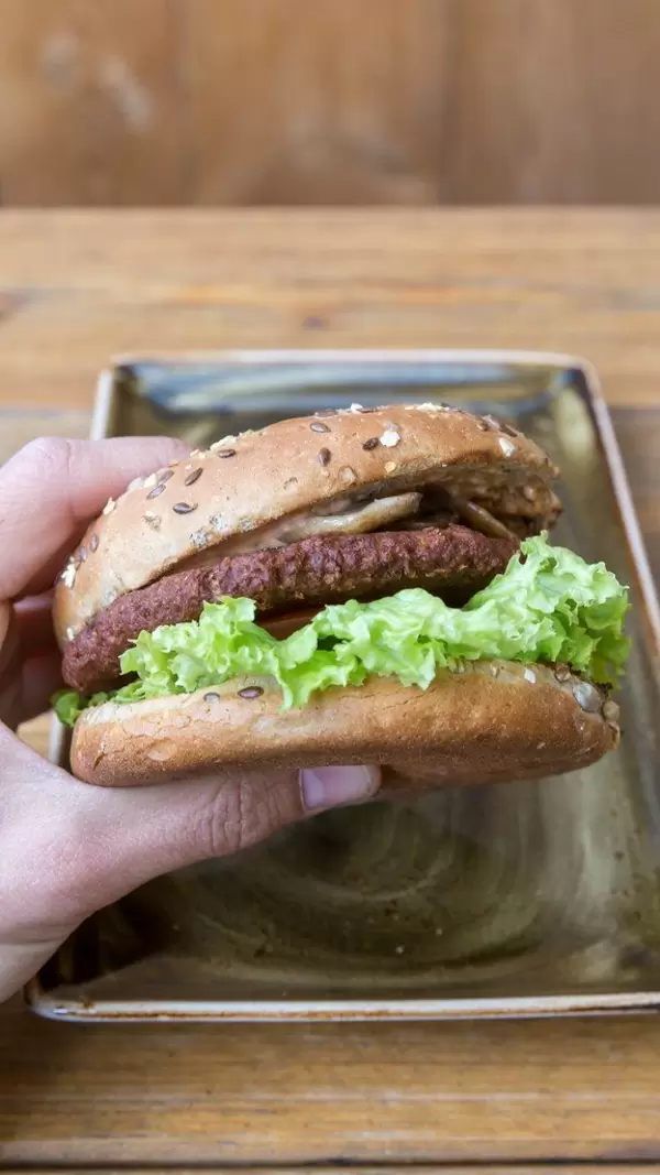 Hand holding the vitamin b12 meatless, vegan  burger "Naturbursche" by Moving Mountains, with caramelised onions, champions, tomatoes and salad
