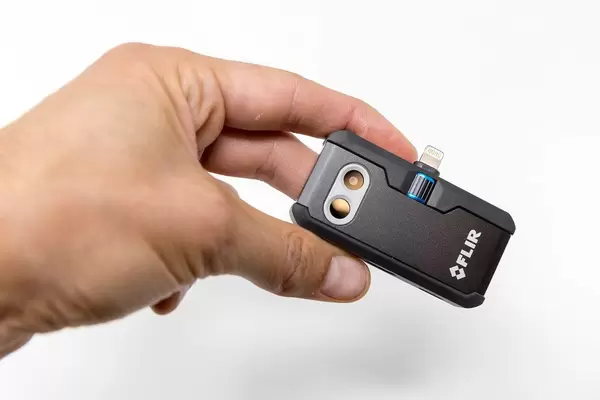 Hand holding thermal imaging / thermographic camera FLIR ONE PRO LT with USB-C port for Android devices, in front of white background