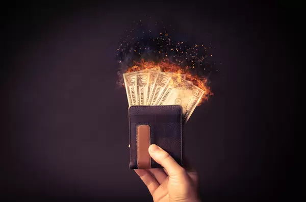 Hand holding wallet with dollar money on fire