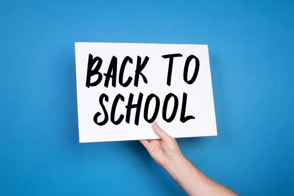 Hand holding white banner with Back to School text on blue background